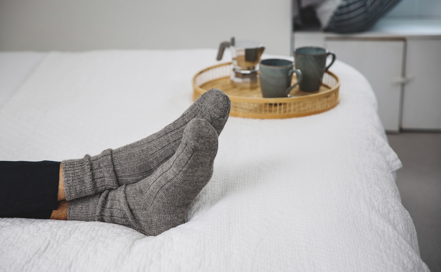 person wearing a pair of lambswool Bed socks while lay down on a bed with a drink. 